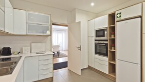 A modern kitchen with white cabinets, a built-in oven, microwave, and a refrigerator. - A modern apartment in Cascais Center (Cascais)