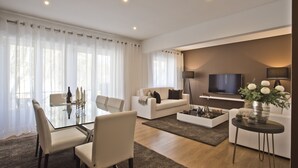A modern living room with a glass dining table, white sofas, a flat-screen TV, and a coffee table. - A modern apartment in Cascais Center (Cascais)