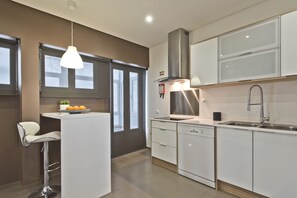 A modern kitchen with white cabinetry, a built-in dishwasher, a stainless steel sink, and a pendant light.