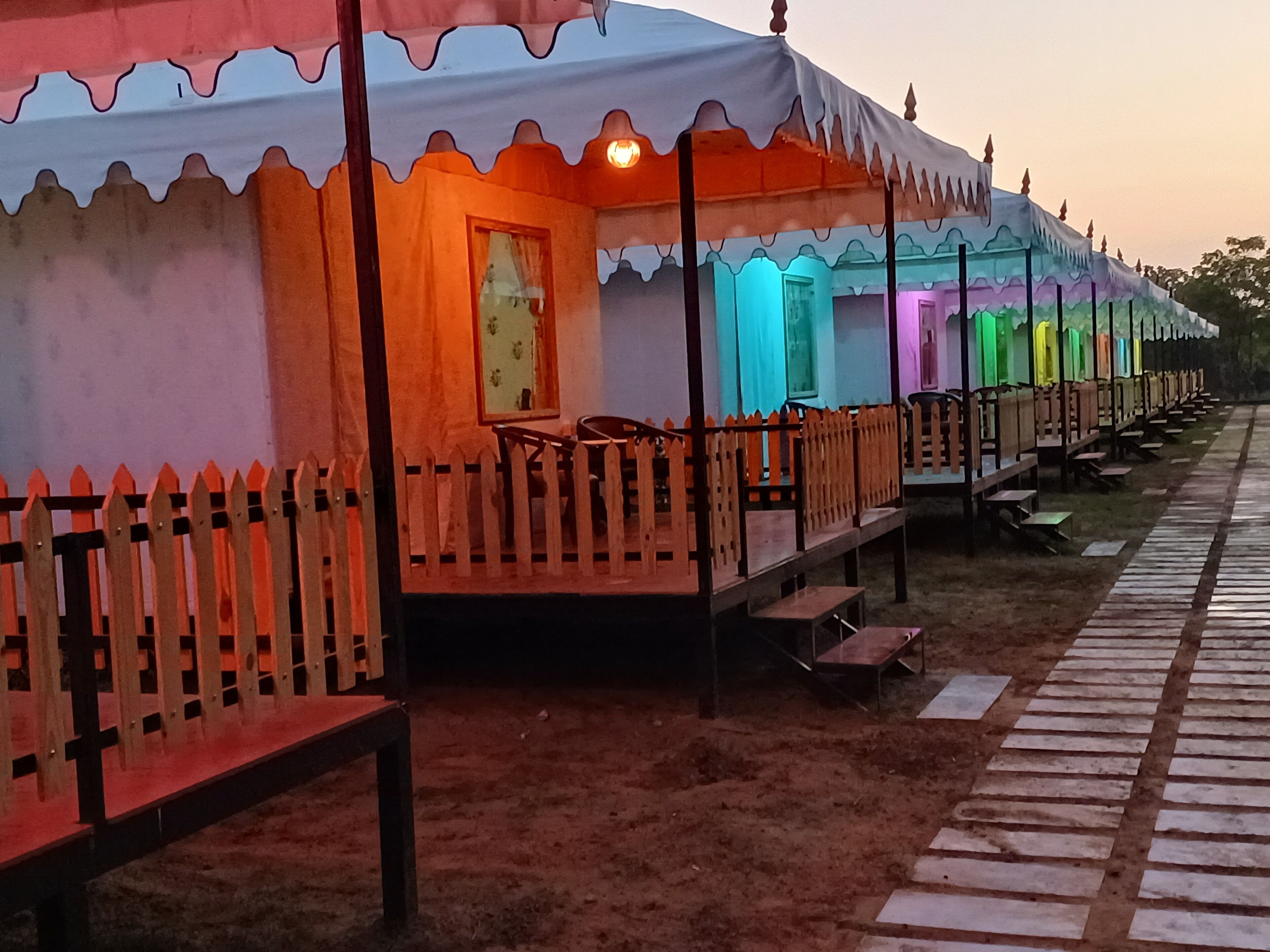 A row of colorful tents with wooden railings and benches, arranged in a linear fashion along a pathway.