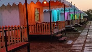 A row of colorful tents with wooden railings and benches, arranged in a linear fashion along a pathway.