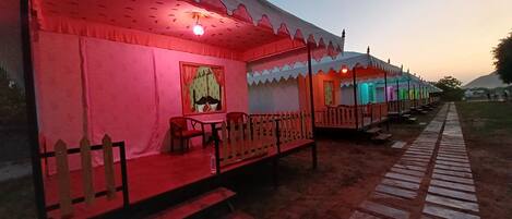 A row of traditional tents with a wooden fence, a bench, and a table with chairs.
