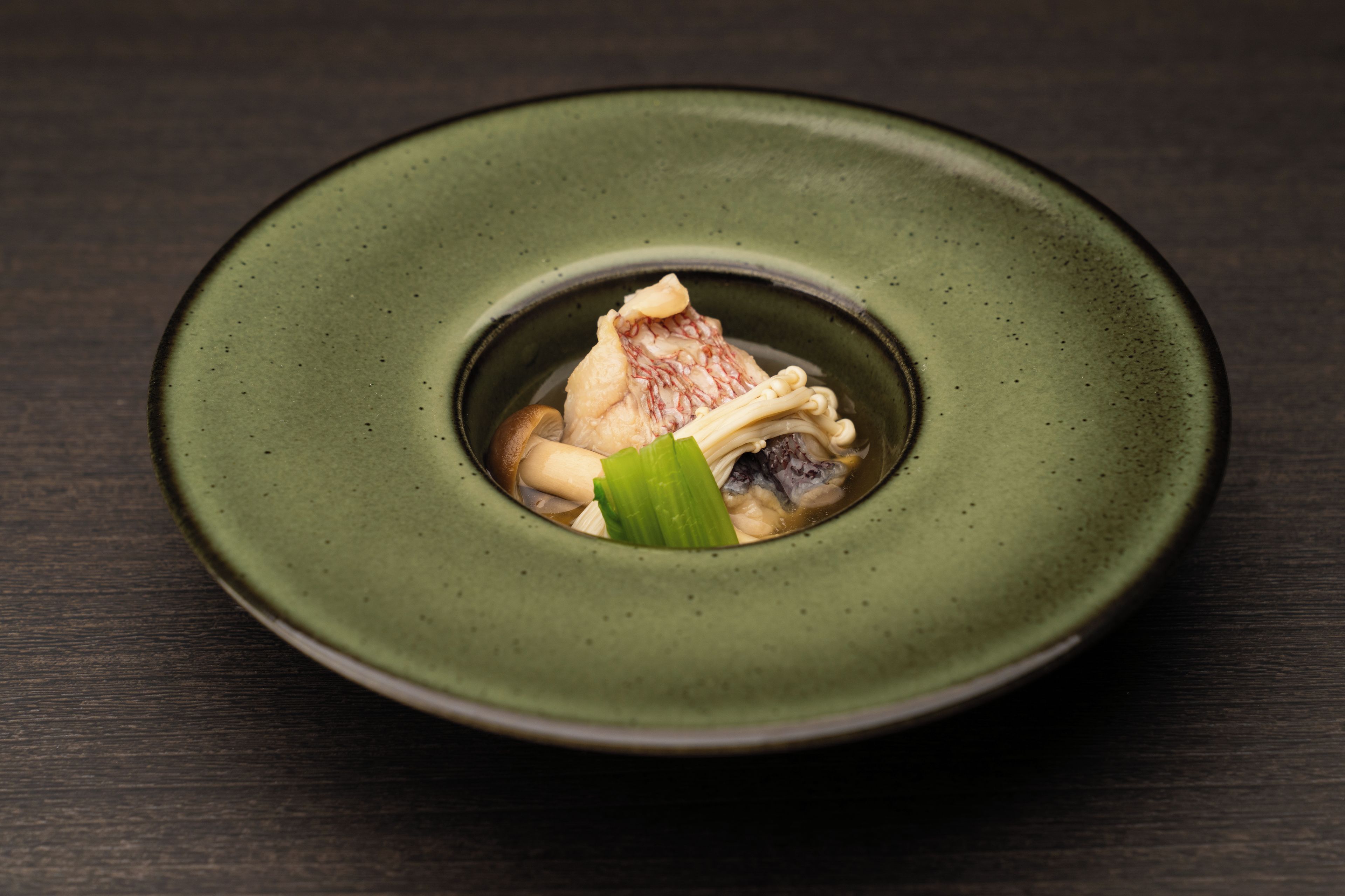 A plate with a green rim containing a dish with a piece of meat, mushrooms, and a green leaf.