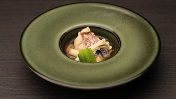 A plate with a green rim containing a dish with a piece of meat, mushrooms, and a green leaf.