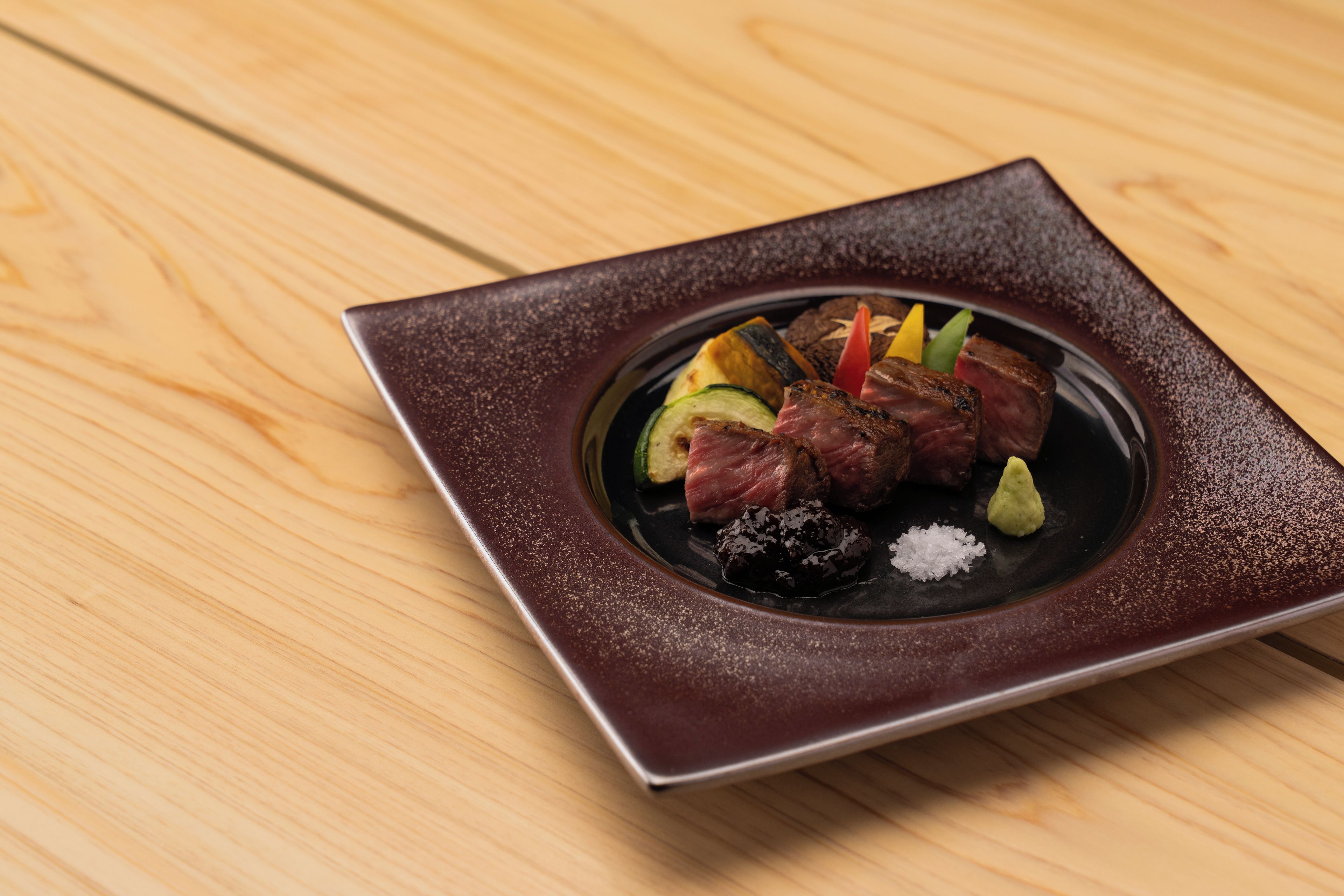 Un plato cuadrado con un borde oscuro sobre una mesa de madera.