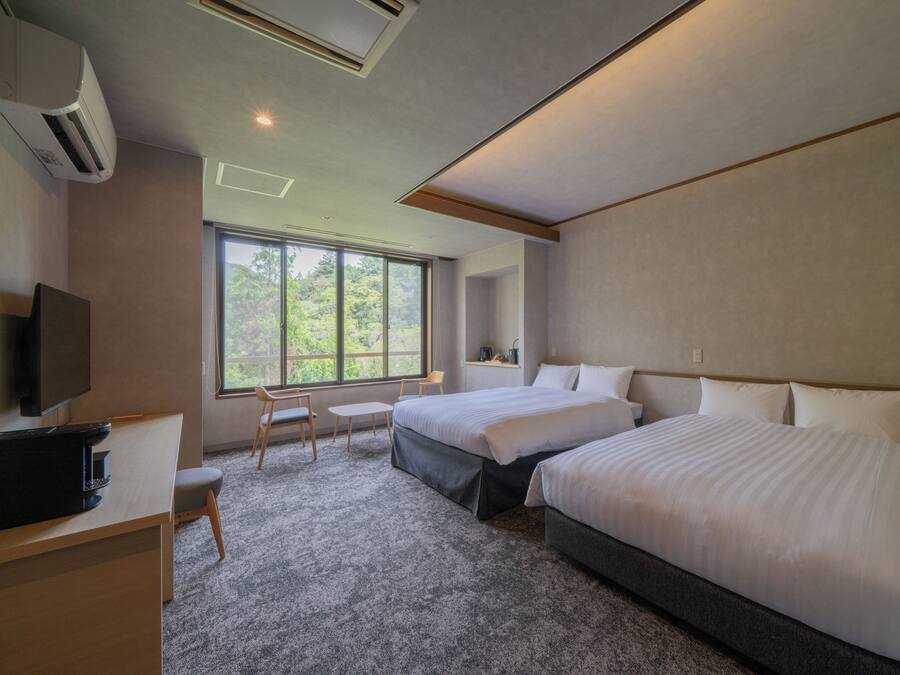 Habitación de hotel con dos camas, un escritorio, una silla y un televisor.