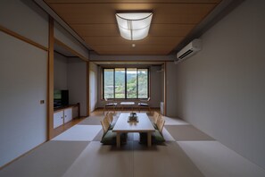 Una stanza in stile giapponese, essenziale, con pavimento in tatami, un tavolino basso e un televisore su un mobile.