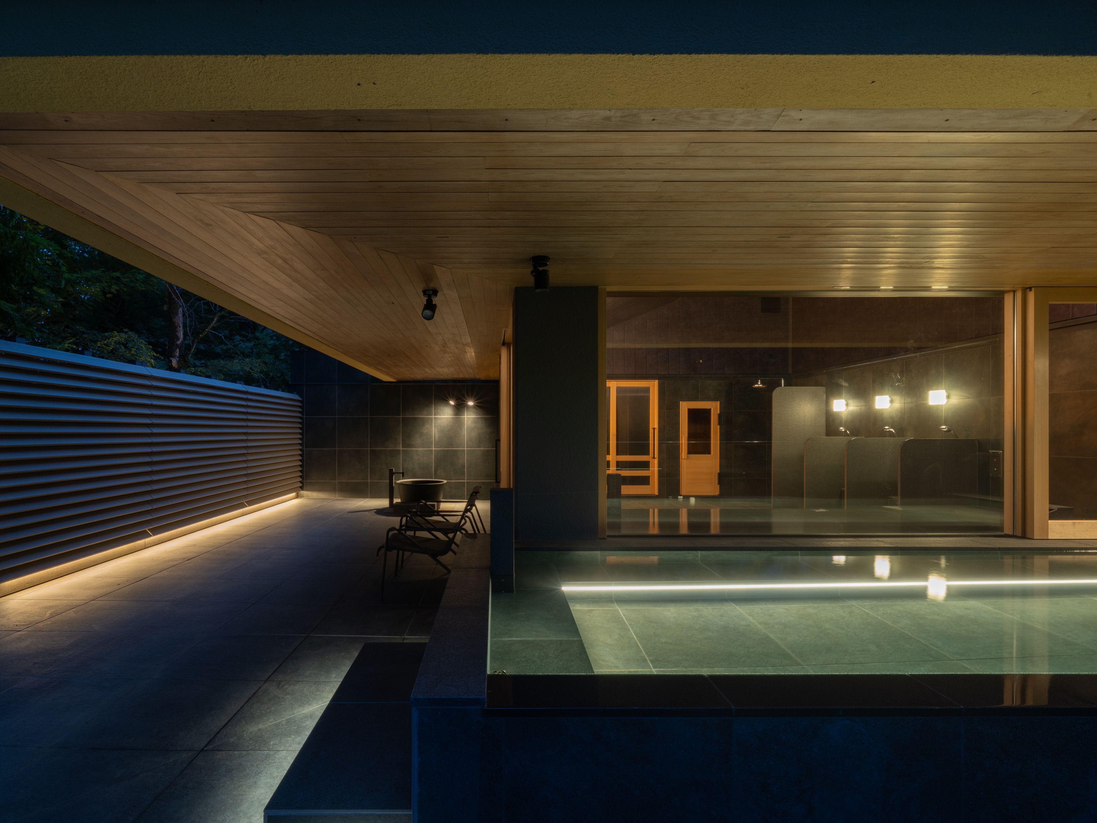 Uma área de piscina moderna ao ar livre, com teto de madeira, estrutura de vidro e espaço para relaxar.
