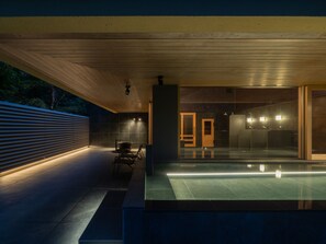 Area piscina esterna moderna con tetto in legno, struttura in vetro e zona relax.