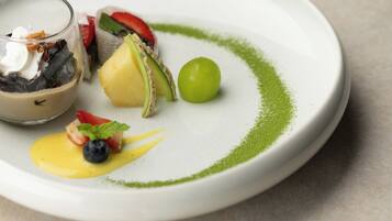 A plate with various food items including a green fruit, a dessert with whipped cream, and a small glass container.