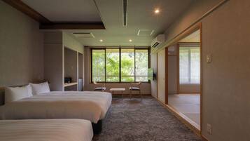 A hotel room with two beds, a desk, and a large window with a view of trees.
