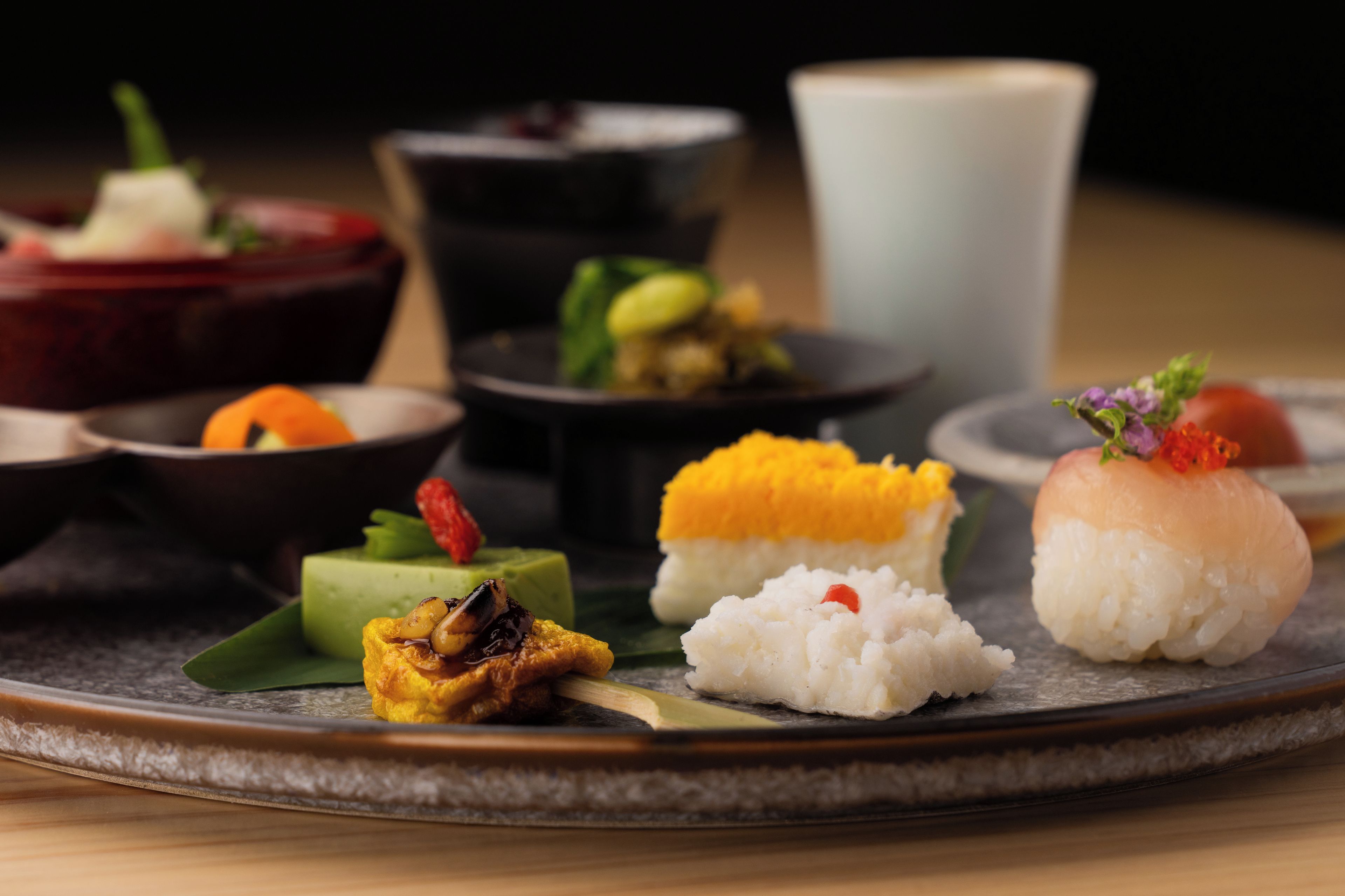 Ett urval av rätter på en mörk tallrik, inklusive sushi och andra asiatiska rätter.