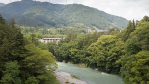 Un río que serpentea por un valle arbolado, con una montaña al fondo y un edificio cerca del río.