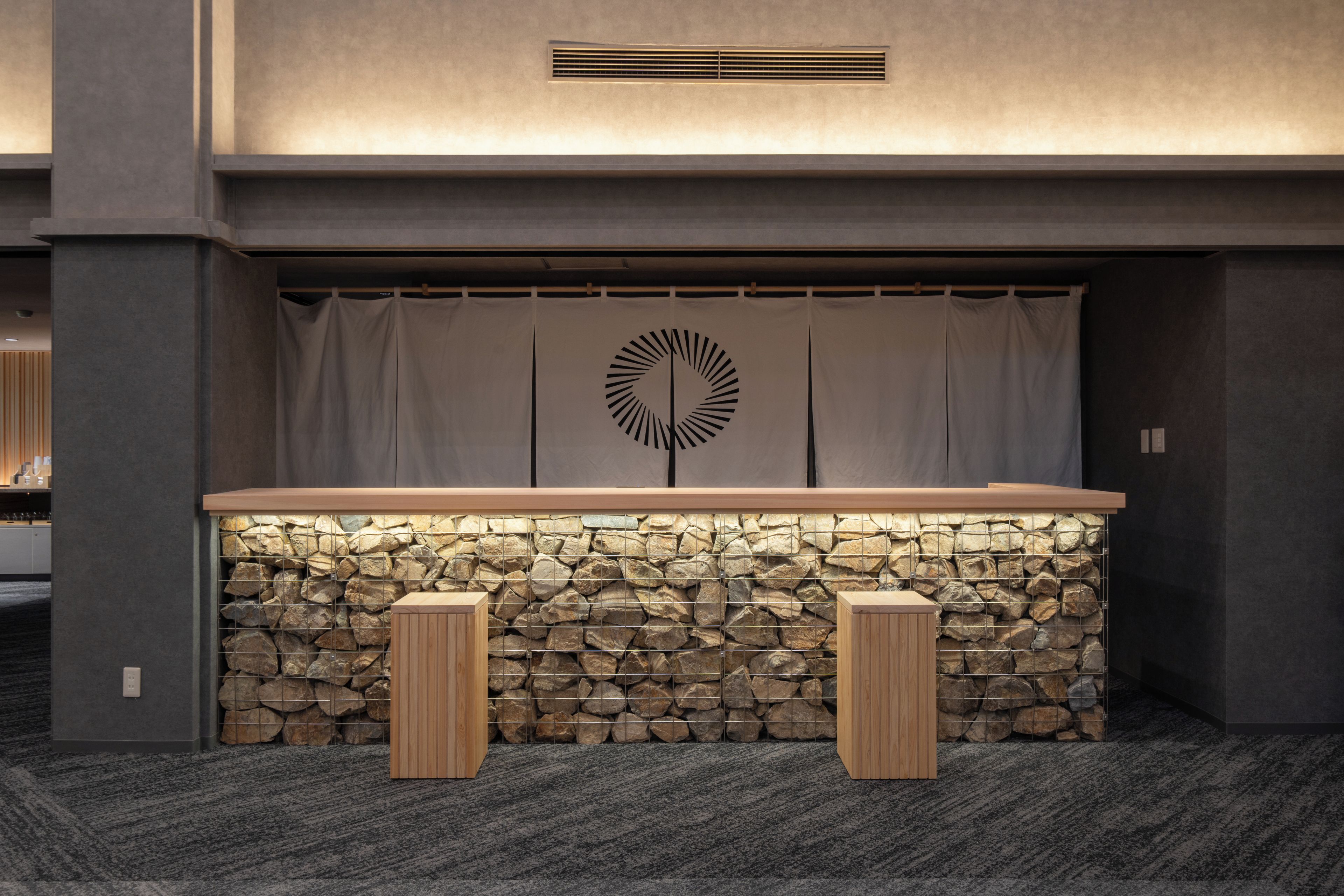 A reception area with a stone wall, a wooden counter, and two wooden stools.