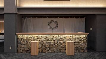 A reception area with a stone wall, a wooden counter, and two wooden stools.
