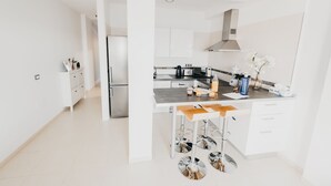 A modern kitchen with white cabinetry, a stainless steel refrigerator, and a bar area with stools.