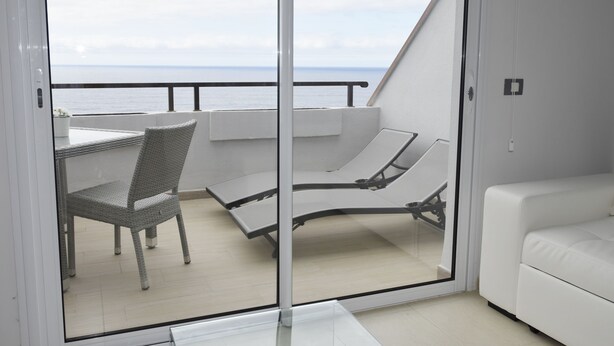 A balcony with a white sofa, a wicker chair, and a glass table.
