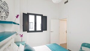 A bedroom with a bed, a window with open shutters, a door, a chair, and a wall decoration. - 1-bedroom in Macarena (Sevilla)