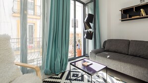 A modern living room with a grey sofa, a glass coffee table, and a view of a balcony with a potted plant. - 1-bedroom in Macarena (Sevilla)