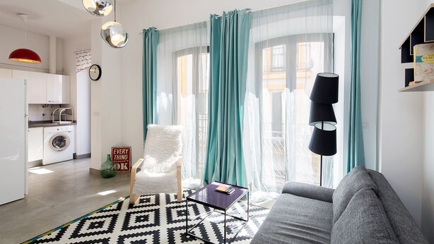 A modern living room with a sofa, a coffee table, and a chair. There is a kitchen area with a washing machine and a refrigerator. - 1-bedroom in Macarena (Sevilla)
