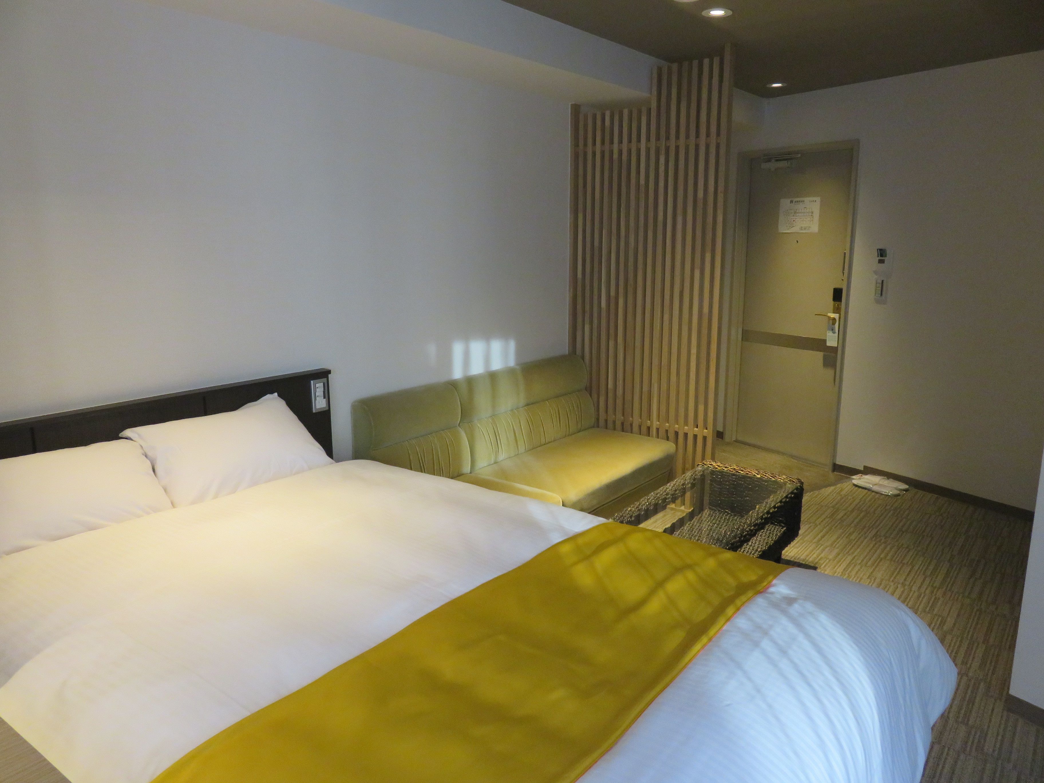 A hotel room with a large bed, a small sofa, a wooden partition, and a door leading to a bathroom.