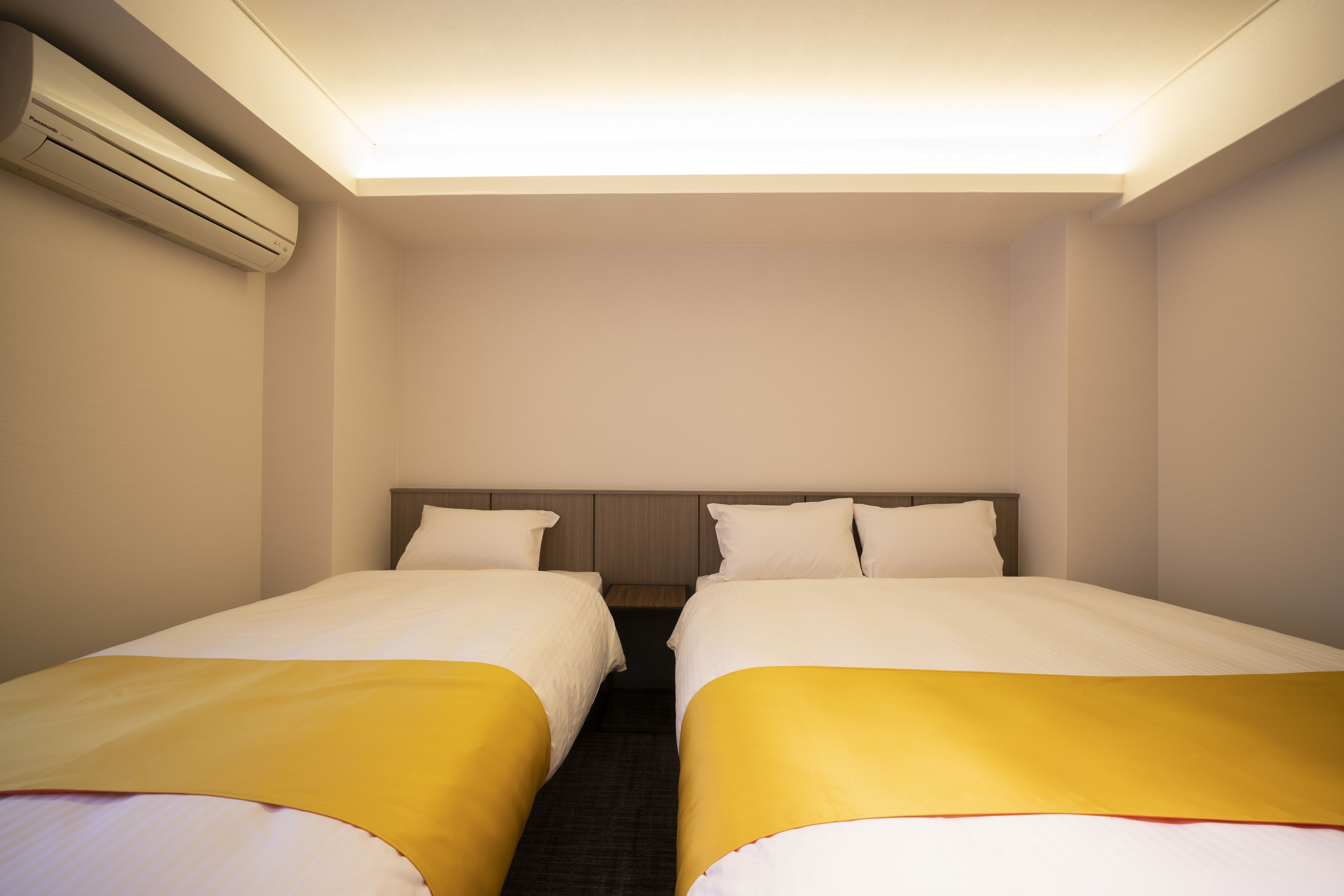A hotel room with two beds, a headboard, and an air conditioning unit.