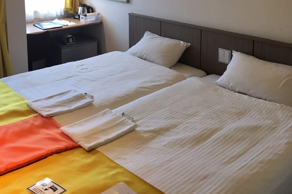 A hotel room with two beds, a desk with a chair, a mirror, and a window with curtains.
