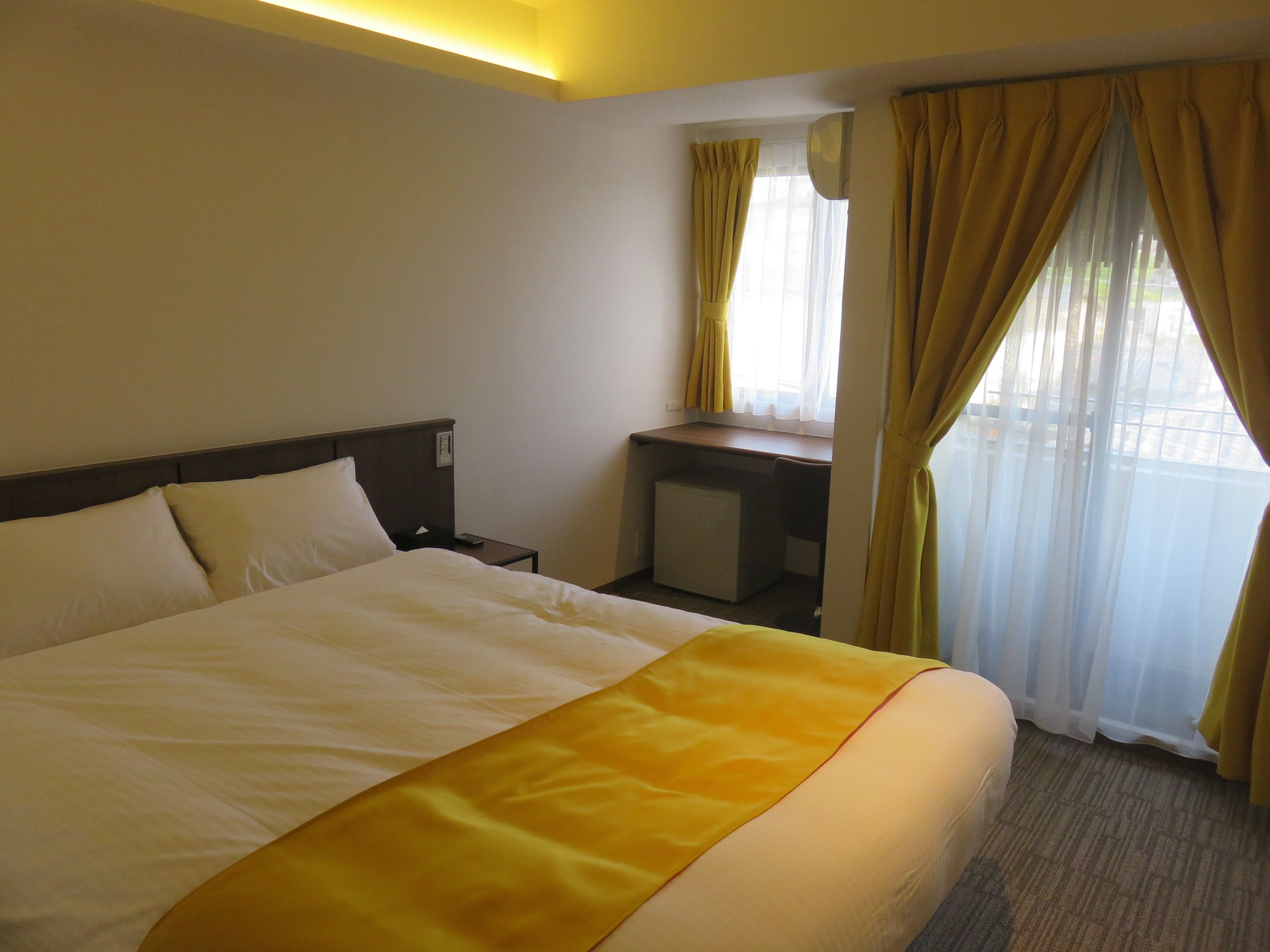 A hotel room with a bed, a desk, and a window with curtains.