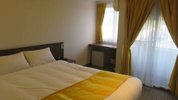 A hotel room with a bed, a desk, and a window with curtains.