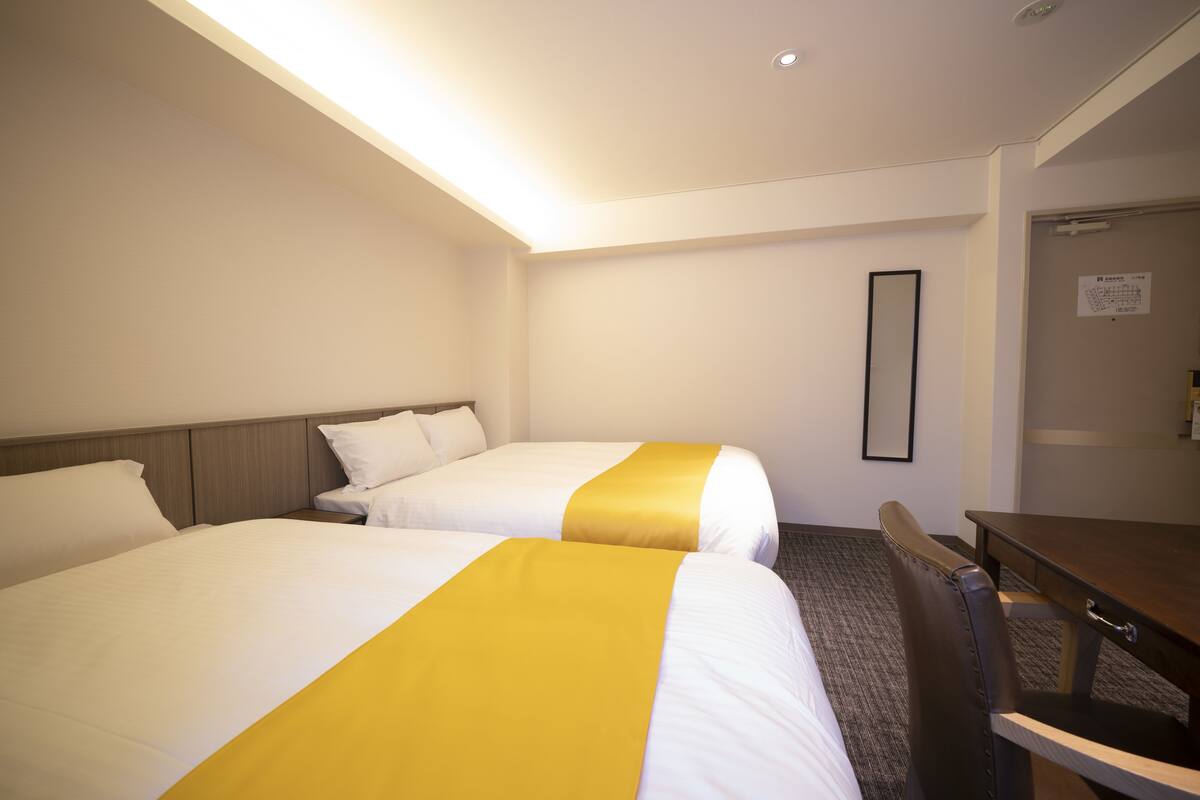 A hotel room with two beds, a desk, and a chair.