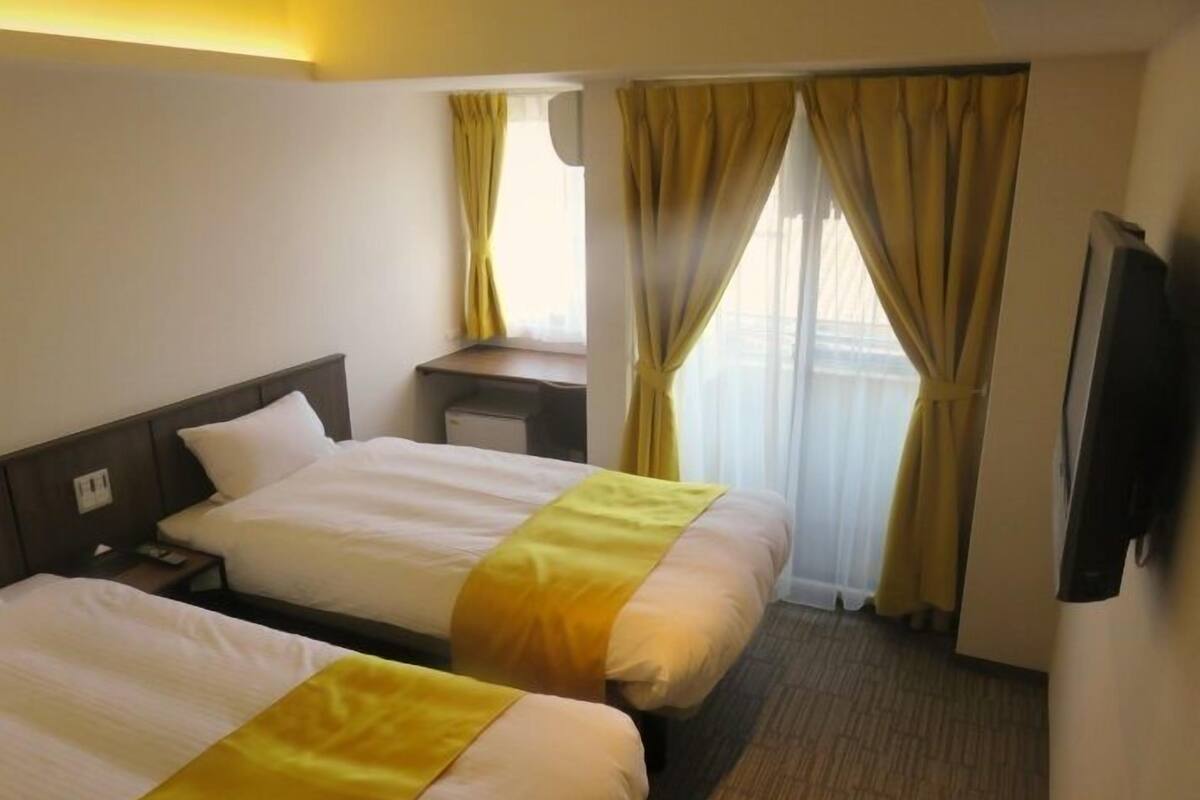 A hotel room with two beds, a desk, a television, and a window with curtains.