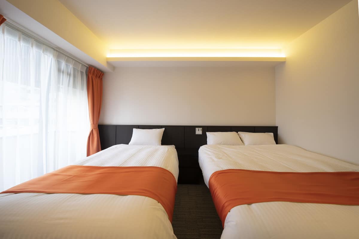 A hotel room with two beds, a headboard, and a window with curtains.