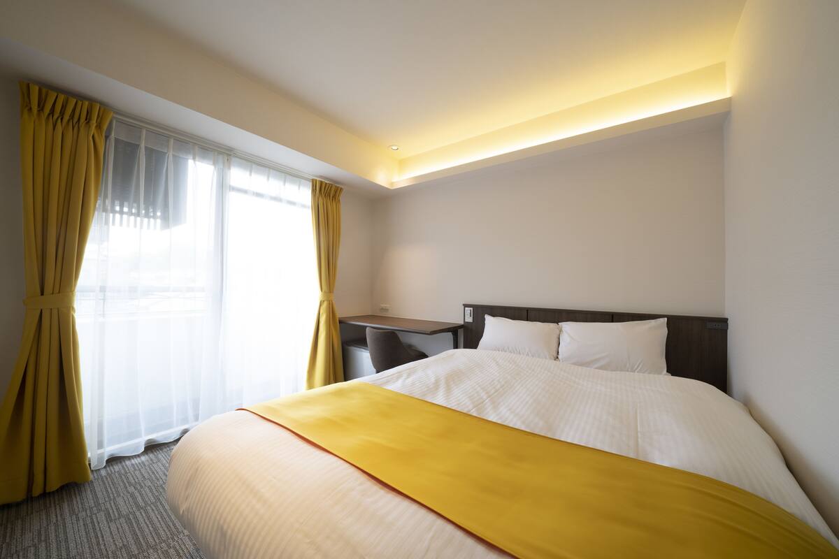 A hotel room with a bed, a desk, and a window with curtains.