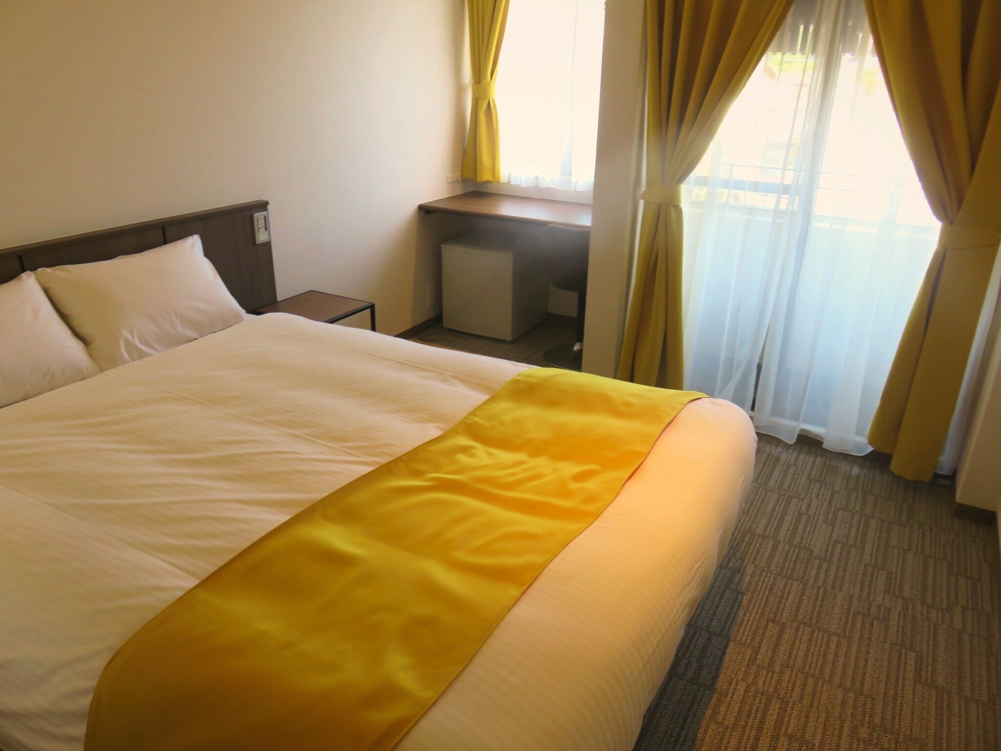 A hotel room with a large bed, a desk, and a view of the outdoors through the window.