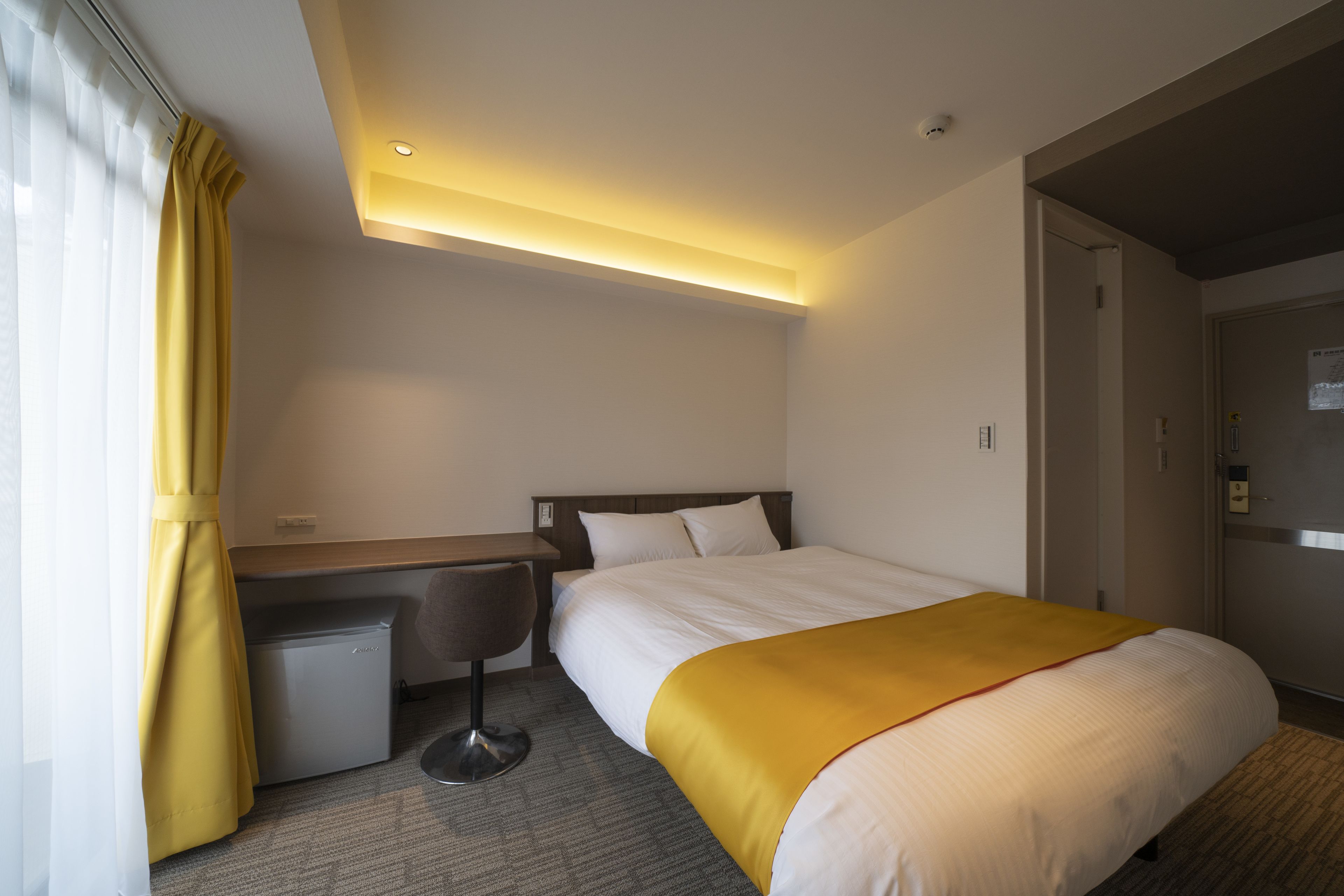 A hotel room with a bed, a desk, a chair, and a small kitchenette.