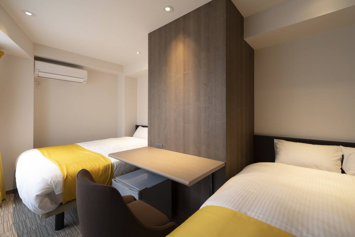 A hotel room with two beds, a desk, and a chair.