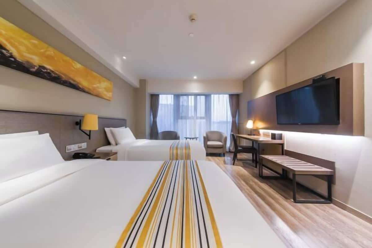 A hotel room with two beds, a desk, a chair, a TV, and a window with curtains.