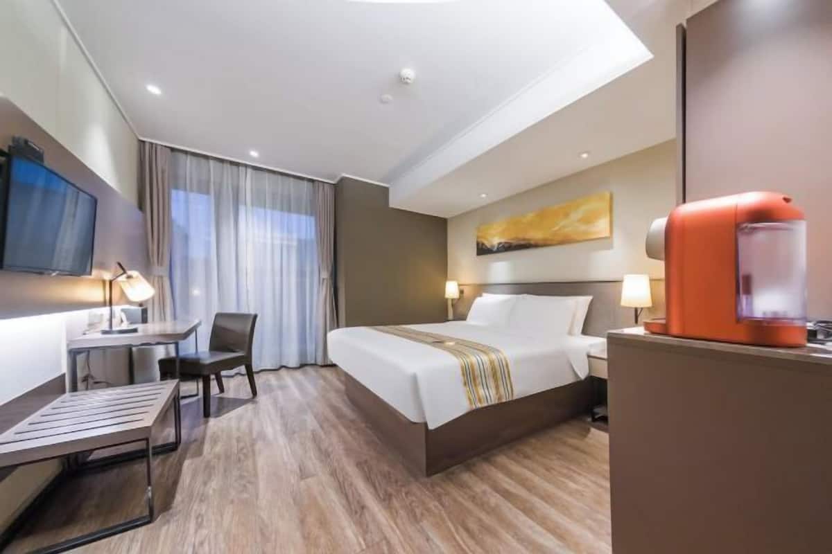 A hotel room with a bed, a desk, a chair, a TV, a painting on the wall, and a water dispenser.
