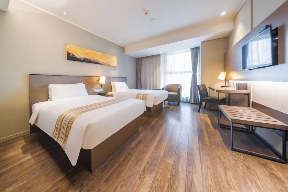 A hotel room with two beds, a desk, a chair, a TV, and a painting on the wall.