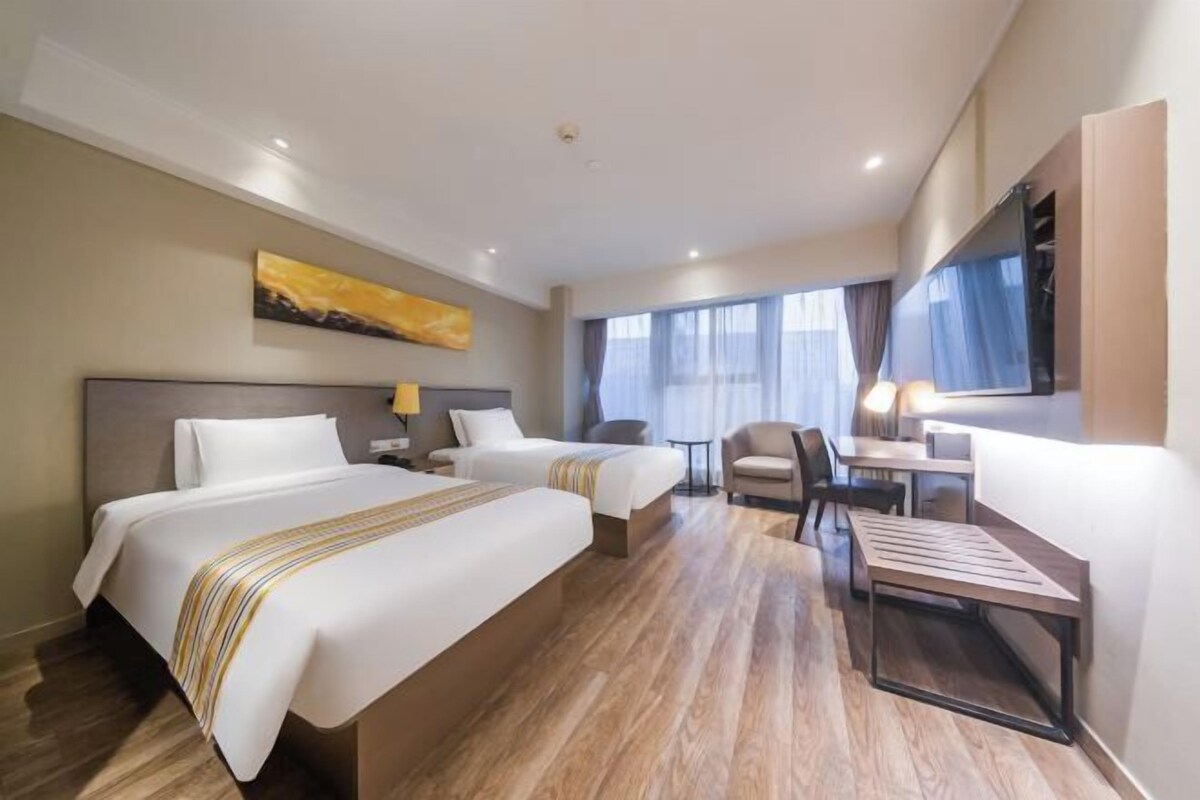 A hotel room with two beds, a desk, a chair, and a TV.