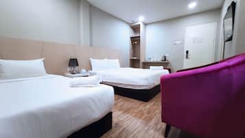 A hotel room with two beds, a wooden floor, a mirror, and a pink chair.