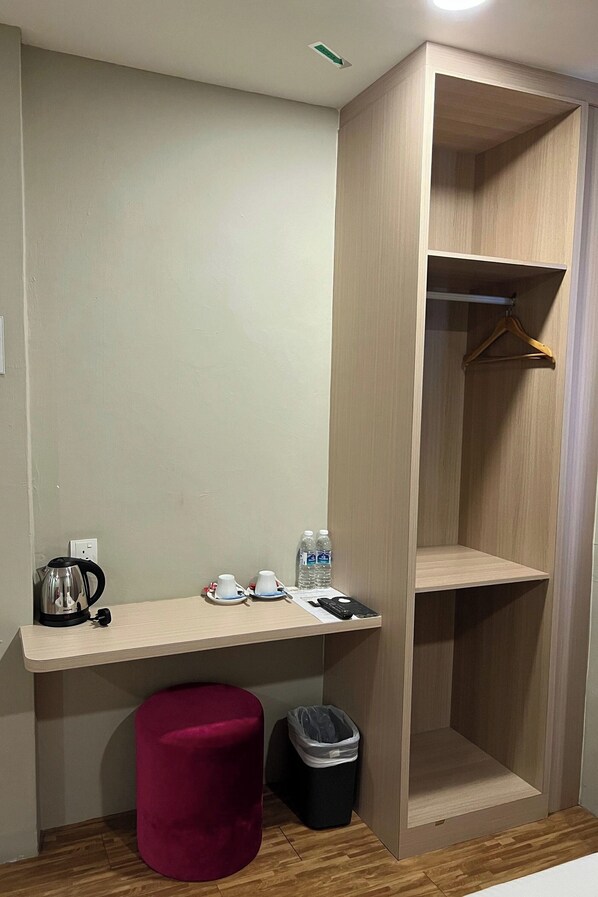 Quarto com escrivaninha de madeira, um banquinho vermelho, um cabide suspenso e um cesto de lixo.