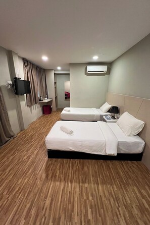 Habitación de hotel con dos camas, un televisor, aire acondicionado, una mesita y un bote de basura rojo.