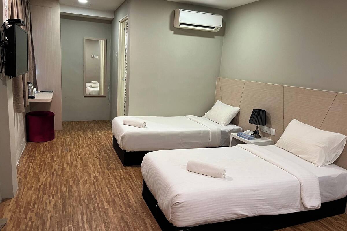 A hotel room with two beds, a desk, a mirror, and an air conditioning unit.