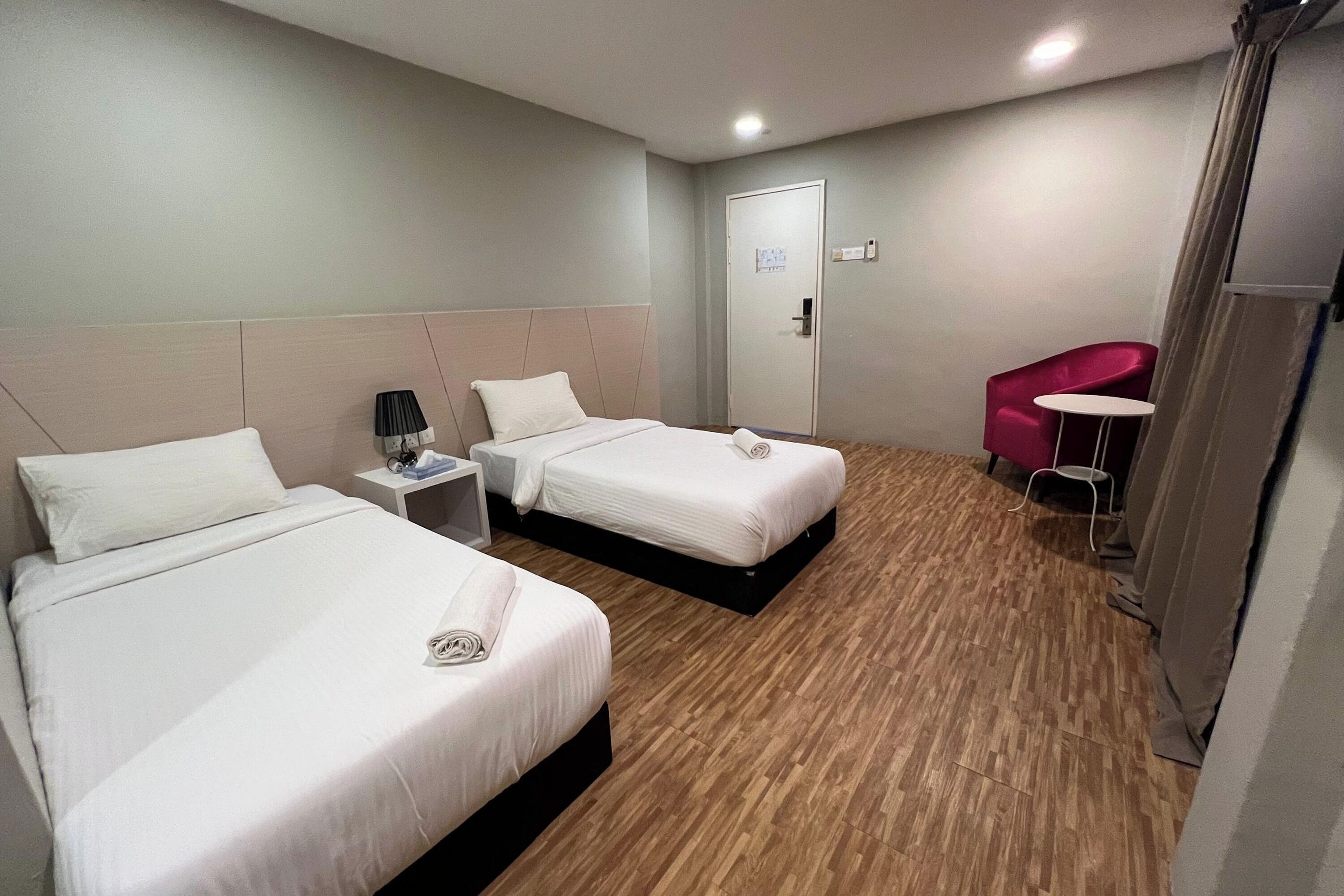 Une chambre d’hôtel avec deux lits, une petite table avec une lampe, une chaise et une porte.