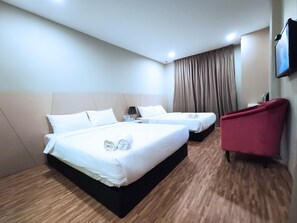 Quarto de hotel com duas camas, uma poltrona vermelha e uma televisão de tela plana.
