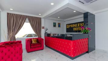 Zona de recepción de hotel con un mostrador rojo, un sofá rojo y una ventana con cortinas.
