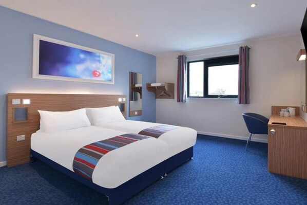 Ein Hotelzimmer mit einem großen Bett, einem Schreibtisch, einem Sessel, einem Fenster mit Vorhängen und einem Gemälde an der Wand.