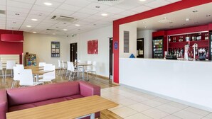 A modern interior with a reception desk, seating area, and a bar. - Travelodge Camberley Central (Camberley)
