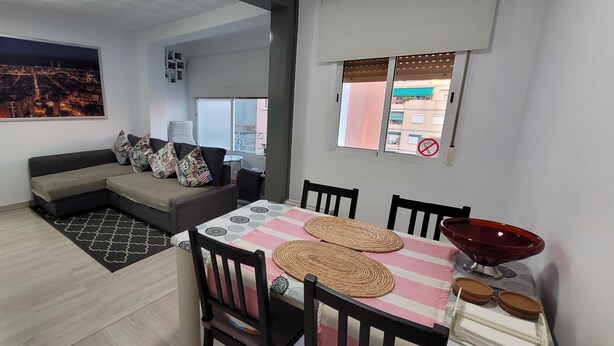 Una sala moderna con un sofá modular, una mesa de comedor con individuales y vistas a la ciudad.